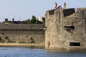 Young people jump from the wall of the fortress surrounding the old town of Ville close into the water of the harbour of Concarneau