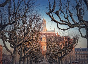 City Hall of Asnieres as seen through the leafless sycamore trees alley outdoors in the park. Asnieres-sur-Seine mairie backyard facade view in sunset light