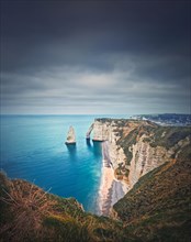 Falaise d'Aval limestone cliffs washed by La Manche channel waters. Beautiful coastline view to the famous rock Aiguille of Etretat in Normandy