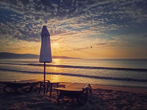 Sunrise at the sea with sunbeds and umbrella on the sandy beach. Summer holiday seaside