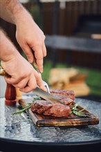 Unrecognizable man cutting freshly grilled beef steak on backyard