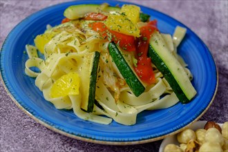 Tagliatelle pasta cooked with vegetables vegan recipe on a blue plate with grated cheese at the bottom