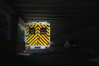 Ambulance or patient transport driving in dark tunnel of a motorway surrounded by moving cars