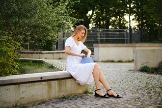 Blonde woman sits on bench and looking for something in her handbag