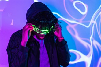 Studio portrait with purple and blue neon lights of a futuristic afro man adjusting an augmented reality goggles