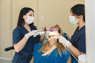 Young woman during teeth whitening procedure with curing UV light at dentist's office
