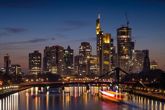 A ship sails on the Main towards Frankfurt's glowing bank skyline in the evening.