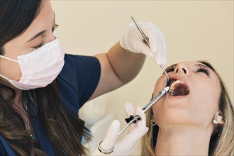 Latina woman dentist administering anesthesia to young blonde patient