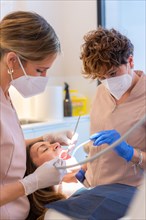 Technician examining the mouth of a woman reclining on chair in a dental clinic