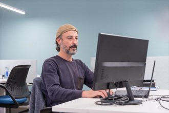 Portrait of a serious stylish mature man sitting on a desk using computer in a co-working