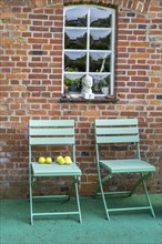 Apples on green garden chair in front of brick wall