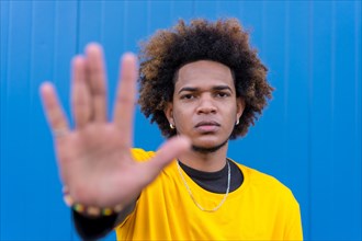 Horizontal photo with blue background of an african american young man gesturing stop with hand