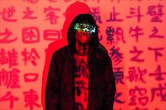 Studio portrait with red neon lights of a futuristic man with AR goggles in a wall with chinese words