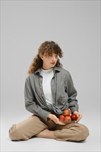 A young woman sits on the floor with a bowl of apples on her knee