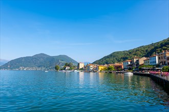 City of Porto Ceresio on Waterfront with Mountain and Lake Lugano in a Sunny Summer Day in Porto Ceresio