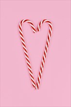 Christmas candy canes forming shape of heart on pink background