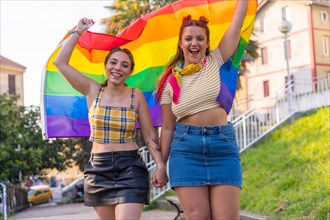 A closeup shot of two young Caucasian hugging females with LGBT pride flag outdoors