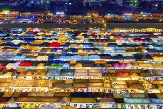 View of rows of colorful outdoor market tents and food stalls at night. Fairs