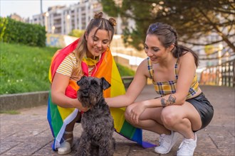 Close-up of two young Caucasian women holding an LGBT pride flag in a park next to their black dog