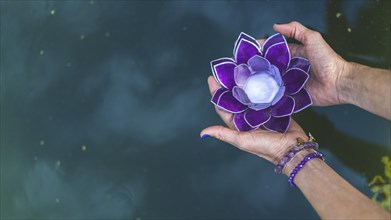 Top angle view of hands holding a purple glass lotus over water. Yoga and meditation concept. Copy space