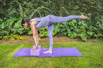 Fit woman in sportswear practices yoga pose using a block outdoors. Yoga with brick