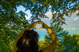 Woman Making a Heart Shape in Front of Lake Brienz with Mountain and Tree Branch in Sunny Summer Day in Brienz