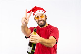 Young very happy Caucasian man with red Christmas hat toasting with a bottle of champagne on a white background