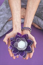 Top angle view of hands holding a purple glass lotus. Yoga and meditation concept. Vertical shot