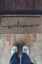 High angle view of welcome mat in door over wooden floor with woman foot-ware near of it