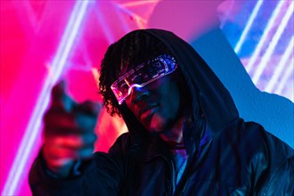Studio portrait with purple and blue neon lights of a futuristic man pointing ahead wearing artificial intelligence goggles