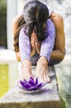 Aesthetic shot of a praying woman sitting behind a purple glass lotus on a tree trunk over the water