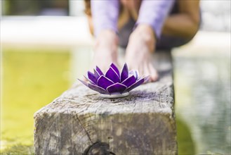 Aesthetic shot of a purple glass lotus on a tree trunk over the water. A praying woman is behind it. Copy space