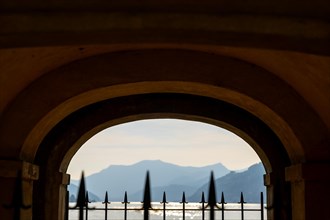 Old Beautiful Street Tunnel with Arch and Spear Fence on the Waterfront in a Sunny Summer Day and with Lake Lugano and Mountain Range in Ticino