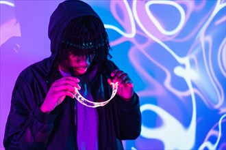 Studio portrait with purple and blue neon lights of an afro man putting on smart goggles