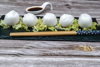 Xiao long bao of prawns on a bed of lettuce on a slate plate with chopsticks and a ceramic spoon with soy sauce