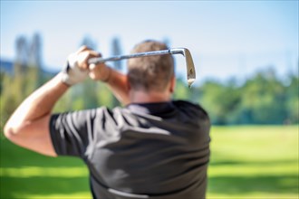 Male Golfer Making a Golf Swing with His 6 Iron Golf Club in a Sunny Day in Switzerland