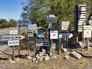 Many different letterboxes and signs are jumbled up on the side of the road