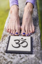 Close up of woman's feet behind an Om sign on a tree trunk over the water