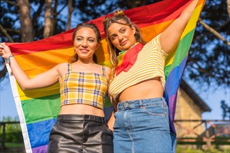 A closeup shot of two young Caucasian females holding LGBT pride flag outdoors