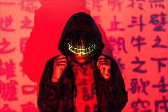 Studio portrait with red neon lights of an anonymous futuristic man wearing smart glasses hiding on a hoodie