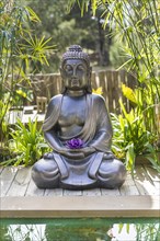 Meditating Buddha Statue with a purple lotus on his hands on a backyard. Vertical shot
