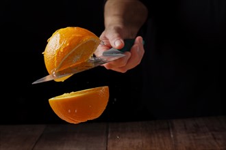Woman cutting an orange in half with a knife in the air spilling water