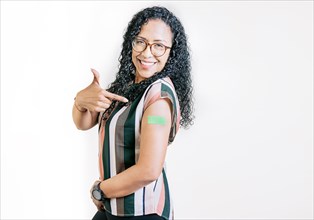 Smiling woman pointing at her vaccinated arm. Latin woman pointing at the bandage on her vaccinated arm