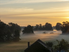 Fog over the meadows at the edge of the village at sunrise