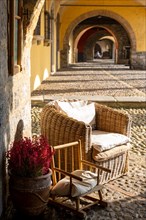 Beautiful Old Narrow Street with Arches and an Armchair with Flowers and Sunlight in Bissone