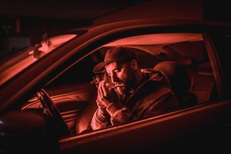 Man in car smoking at night in a garage lit with a red light