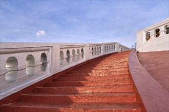 Red sunlit stairs and white banisters leading upwards at blue sky. Concept of ascension