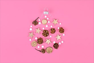 Seasonal ornaments like natural hernlock cones and stick slices with stars and white snowballs forming shape of Christmas tree bauble on pink background