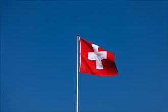 Beautiful Swiss Flag Against Blue Clear Sky in a Sunny and Windy Day in Switzerland