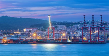 View of Lisbon port with moored sea container ship with port cranes in the evening twilight over Tagus river. Lisbon
